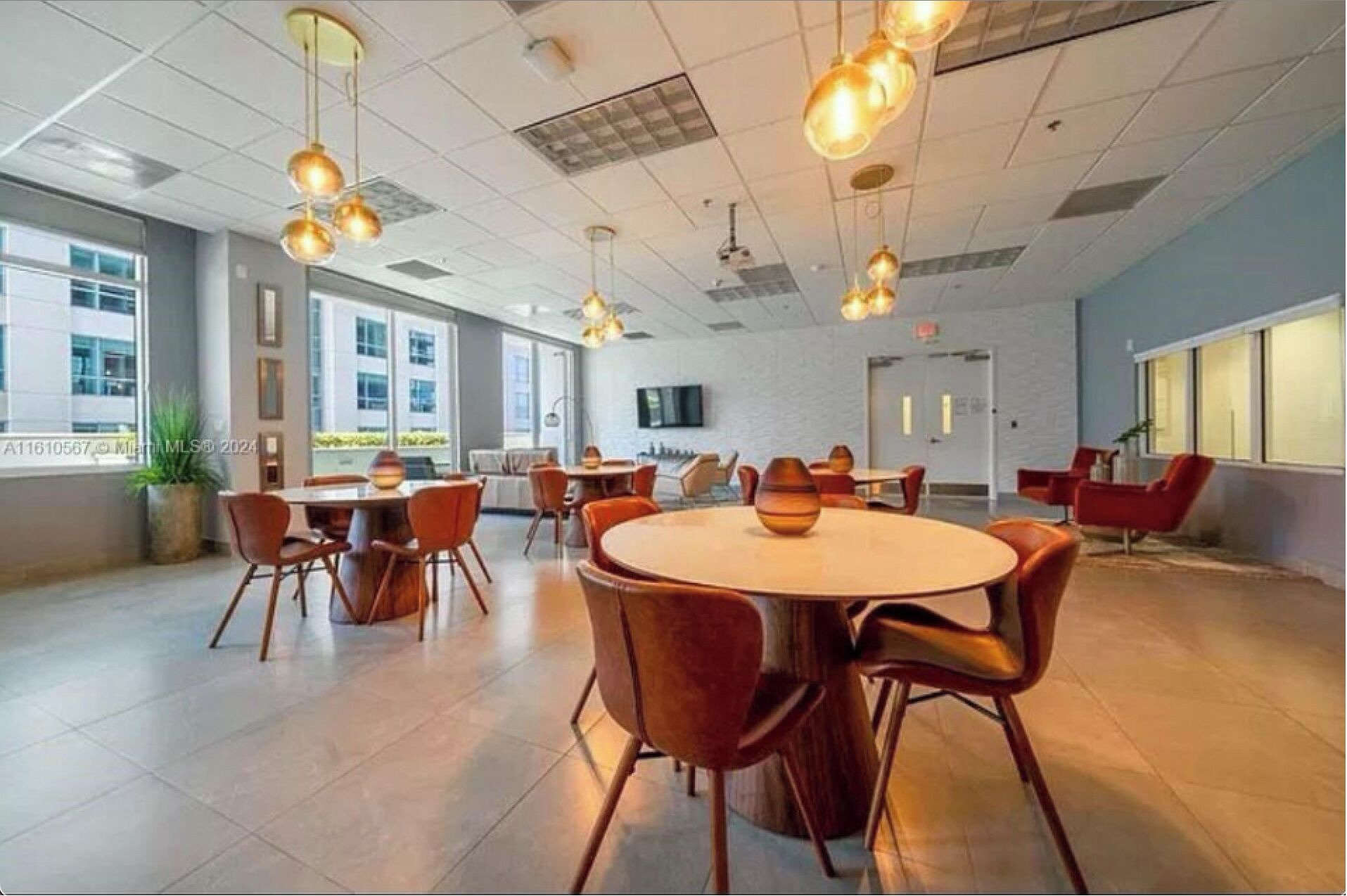 A modern conference room with round tables and chairs, large windows, and hanging pendant lights.