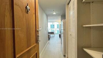 A hallway with a wooden door, a white closet with shelves, and a view into a room with a bed and a window.