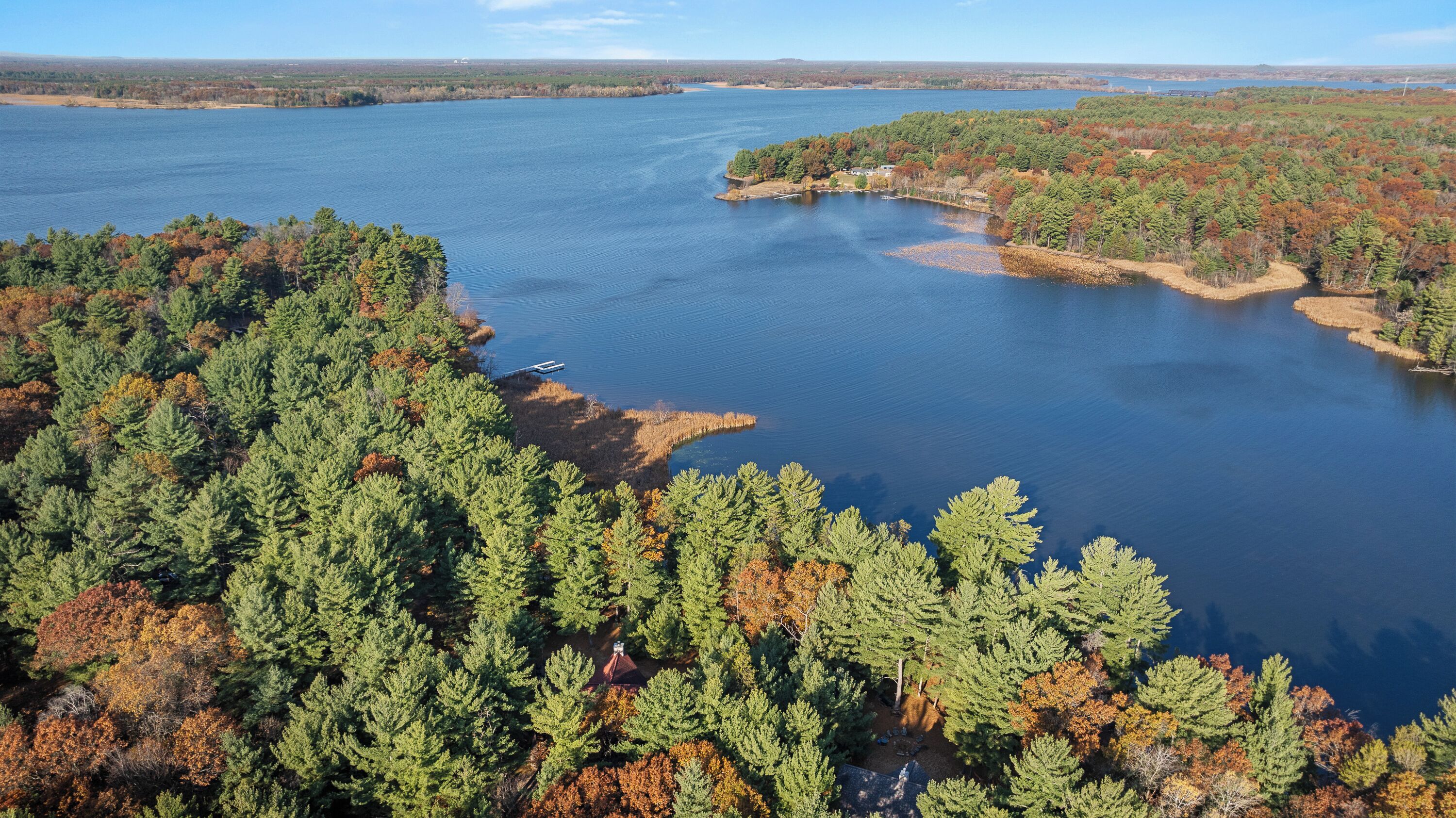 An aerial view of a lake surrounded by dense forests with a small dock and a boat.