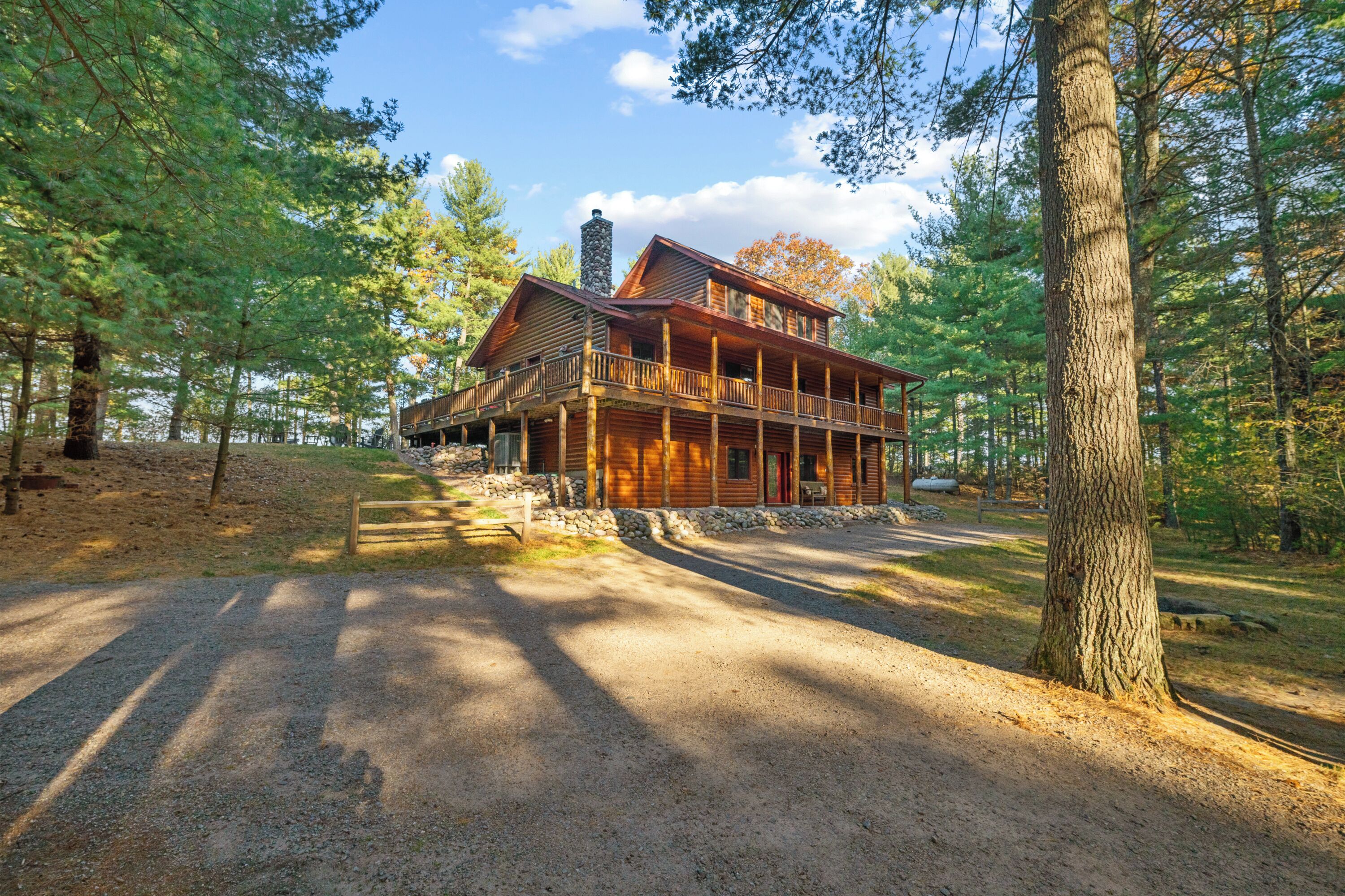 Une cabane avec une façade en bois, une cheminée en pierre et une véranda dotée de balustrades.