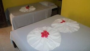 Two single beds with white bedsheets and red flowers, a small table, and a yellow wall. - Pousada Vila do Zimbo (Cairu)