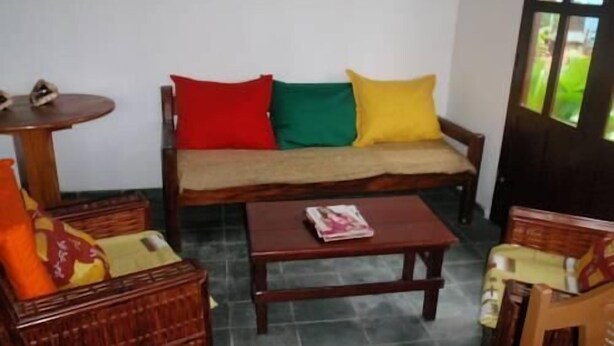 A room with a wooden sofa with colorful cushions, a small wooden table, and wicker furniture. - Pousada Vila do Zimbo (Cairu)