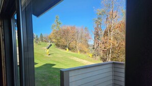 A view from a balcony with a wooden deck, overlooking a grassy yard with trees and a clear sky. - Cozy condo, Family- friendly just completely remodeled. SKI IN -SKI OUT!! (Champion)