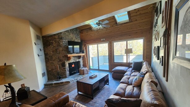 A cozy living room with a stone fireplace, leather sofa, and a large window overlooking a deck. - Cozy condo, Family- friendly just completely remodeled. SKI IN -SKI OUT!! (Champion)