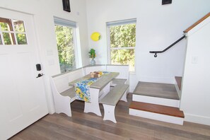 A room with a bench and table, a staircase, and a view of greenery outside.