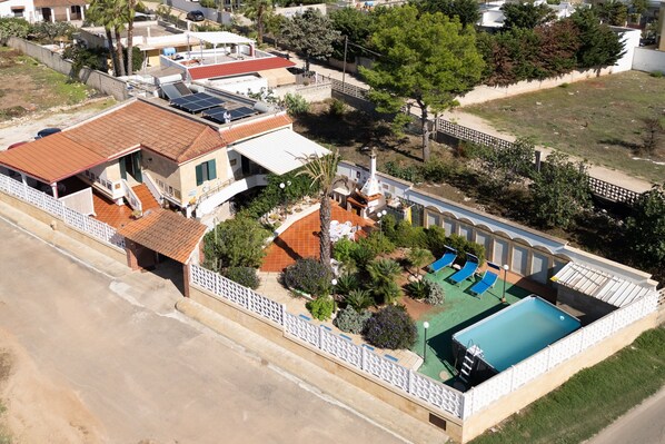 An aerial view of a residential property with a swimming pool, solar panels, and a fenced garden area.