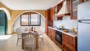 A kitchen with a dining table, chairs, wooden cabinets, a refrigerator, and a window with a view. - Villa 'Malva House In  Con Piscina' with Shared Pool, Wi-Fi and Air Conditioning (Scala di Furno)
