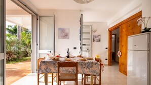 Un comedor con una mesa dispuesta para cuatro personas, un refrigerador y una puerta que da a un jardín.
