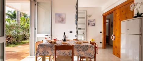 A dining area with a table set for four, a refrigerator, and a door leading to a garden.