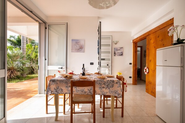 A dining area with a table set for four, a refrigerator, and a door leading to a garden.