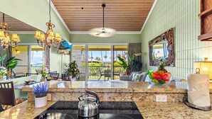 A modern kitchen with a black induction cooktop, a kettle, and a countertop with a bowl of fruit.
