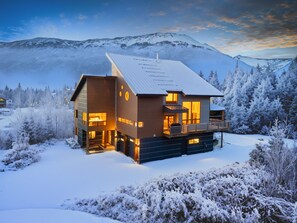 A modern two-story lodge with a large deck and a ski lift in the background.