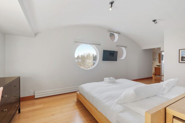 A bedroom with a bed, a dresser, a TV mounted on the wall, and a window.