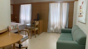 A living room with a green sofa, a wooden dining table with chairs, and a TV on a wooden stand. - Flat na rua Bela Cintra (São Paulo)
