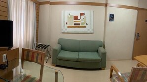 A living room with a green sofa, a glass coffee table, striped chairs, a TV, and a painting on the wall. - Flat na rua Bela Cintra (São Paulo)