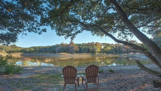 Two wooden Adirondack chairs facing a lake with a forested hill in the background. - 2507 - Salty Sandpiper - Coastal Retreat in Duck | Hot Tub & Sunsets (Duck)