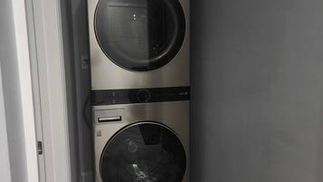 Una lavadora secadora de acero inoxidable, con dos puertas, montada en la pared en una esquina, sobre piso de baldosas.