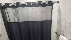 A bathroom with a shower curtain, a toilet, and a towel rack. - Majestically Pleasant Suite (Hempstead)