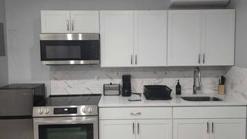 Una cucina moderna con mobili bianchi, un forno a microonde in acciaio inossidabile, un forno integrato, una macchina da caffè e un lavello.