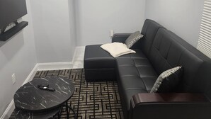 A modern living room with a black leather sofa, a marble coffee table, and a flat-screen TV mounted on the wall. - Majestically Pleasant Suite (Hempstead)