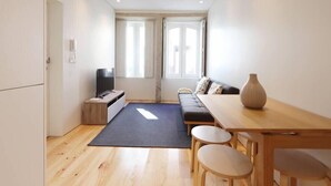 A compact living space with a sofa, a dining table with chairs, a TV, and a large vase. - HM - Pinheiro Duplex Apartment (Porto)