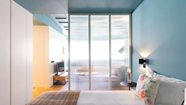 A modern hotel room with a large bed, a TV, and a view through a sliding door to a balcony. - HM - Infante Riverside Apartment M (Porto)