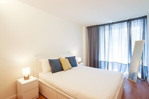 A neatly arranged bedroom with a bed, bedside tables, and a large window with curtains.