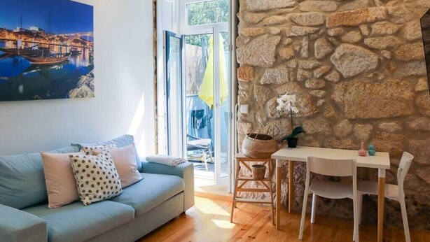 Un salon chaleureux avec un canapé bleu clair, une table à manger entourée de chaises blanches, un mur en pierre et un tableau représentant un paysage urbain.