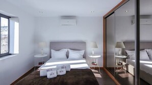 A modern hotel room with a large bed, two bedside tables with lamps, a large mirror, and a view of the city. - Panoramic River View Downtown With Terrace (Porto)