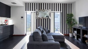 A modern living room with a grey sectional sofa, a large mirror, and a black and white striped wall. - Panoramic River View Downtown With Terrace (Porto)