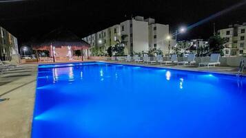 Una piscina notturna con acqua cristallina, circondata da sdraio e un'area coperta.