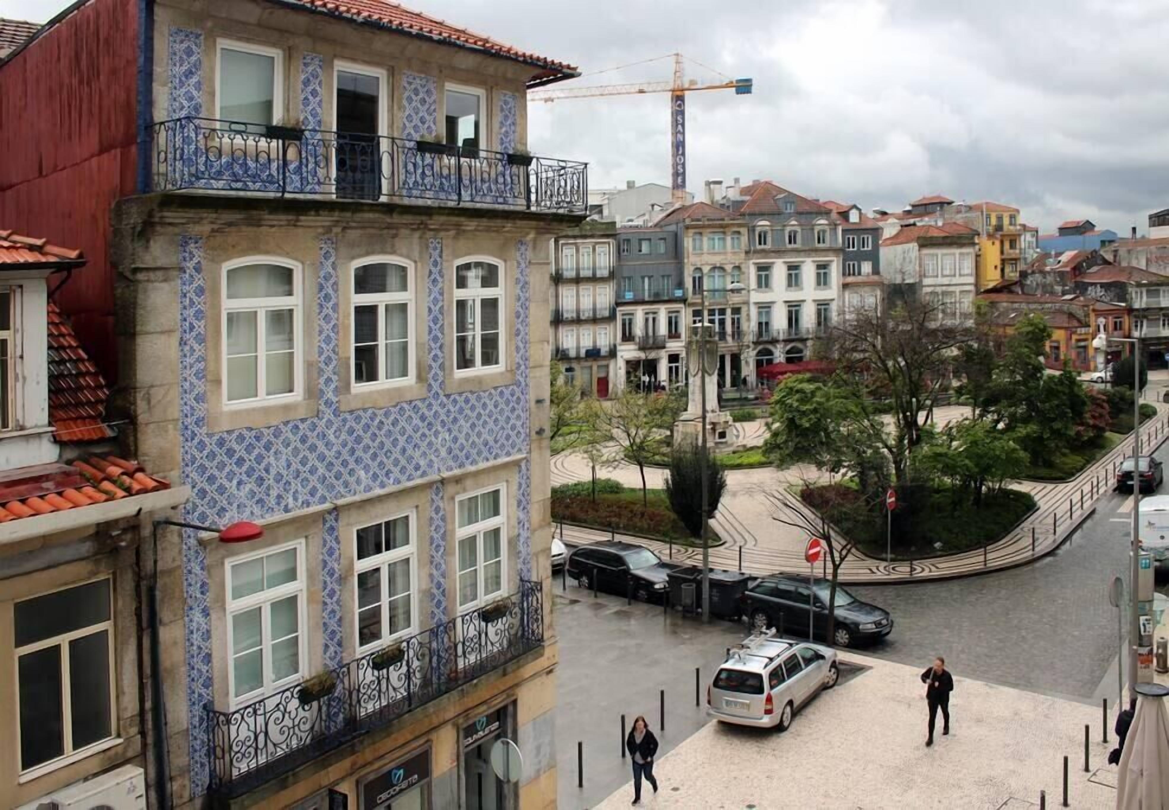 Un edifici de diverses plantes amb façana blava i blanca, un balcó amb barana negra i una entrada a la planta baixa ben visible.