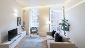 Una sala de estar moderna con un televisor de pantalla plana, un sofá, un sillón y un ventanal con vistas a edificios.