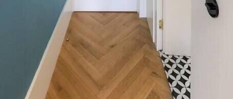 Un pasillo con piso de madera en espiga, una puerta blanca y una pared azul.