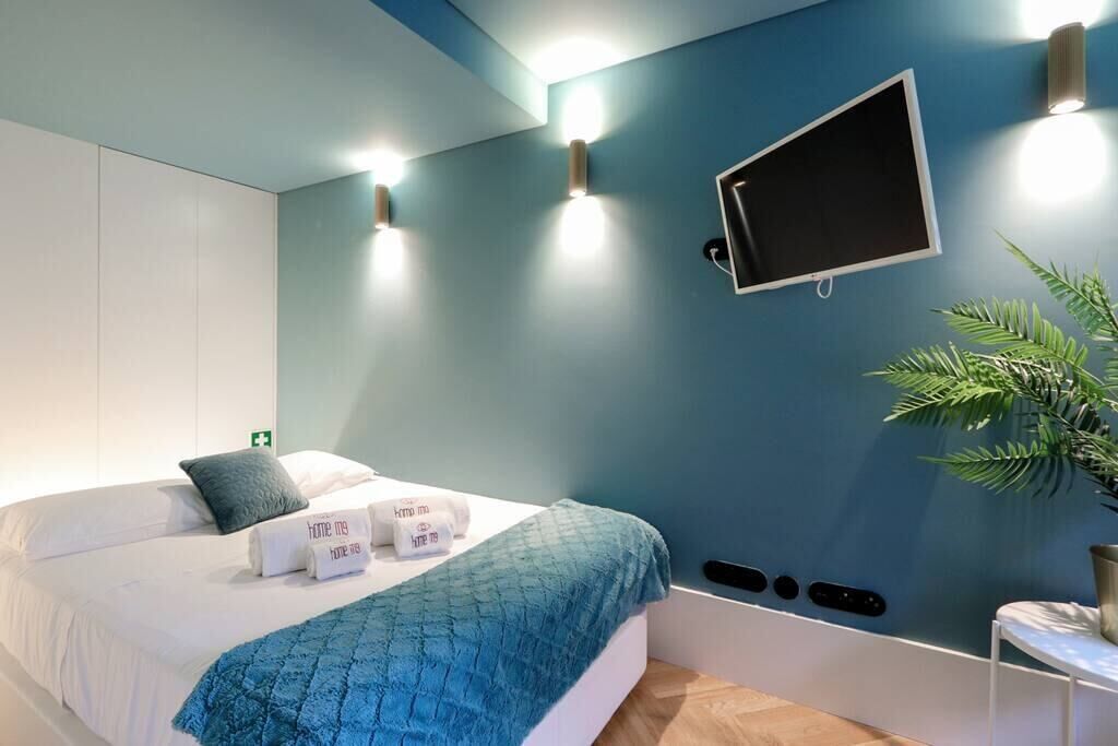 Een moderne slaapkamer met een bed, een wandtelevisie, wandlampen, een plant en een nachtkastje.