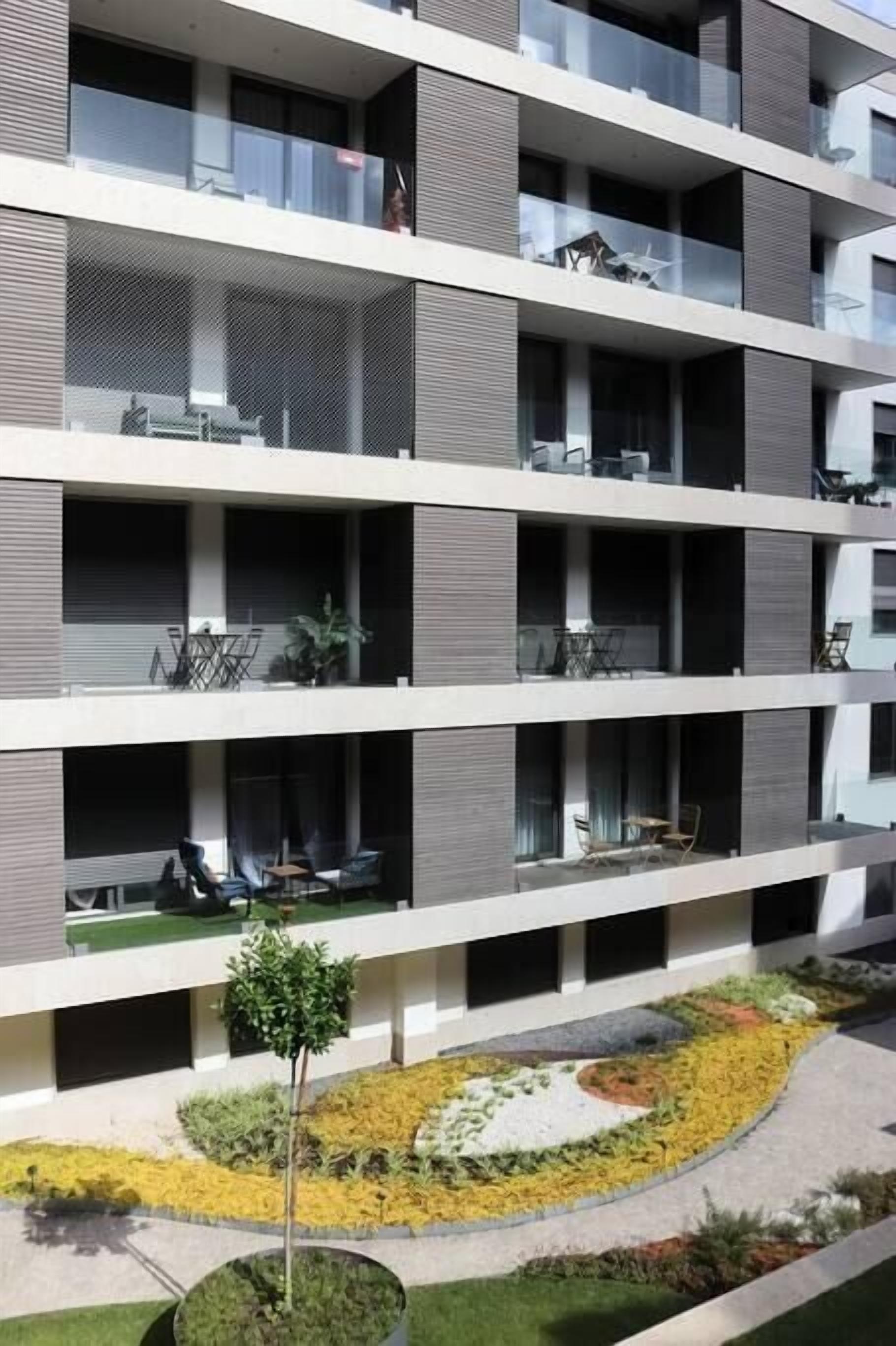 Un edificio residenziale a più piani con balconi, area salotto esterna e giardino curato.