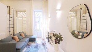 Ein modernes Wohnzimmer mit einem grauen Ecksofa, einem gemusterten Teppich, einem weißen Konsolentisch mit Blumenvase und einem großen Spiegel an der Wand.