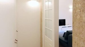 Ein schmaler Flur mit Holzboden, der zu einem Raum mit einer weißen Tür und einer modernen Lampe führt.