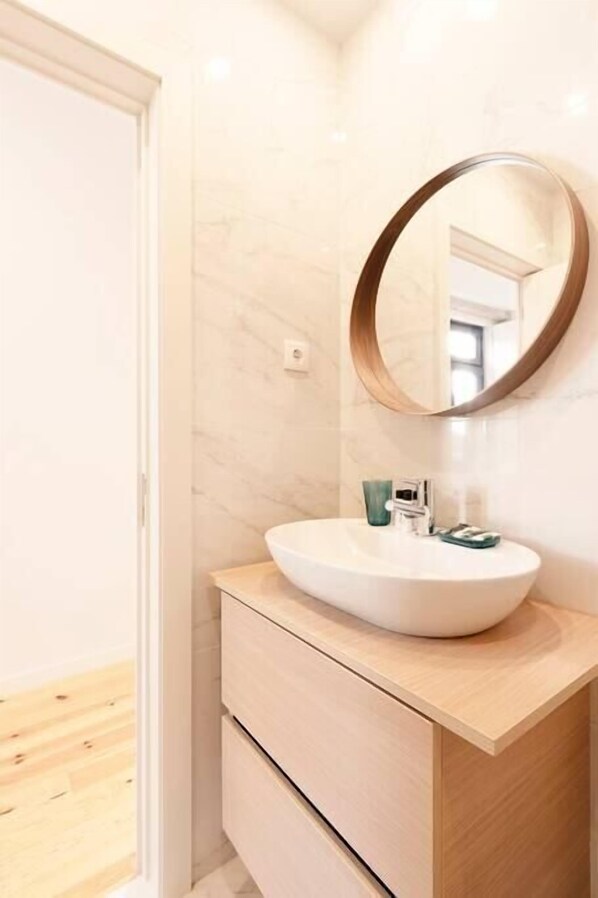 A bathroom with a white sink, a wooden vanity, and a round mirror.
