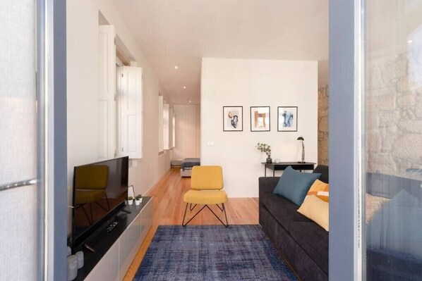 Una sala moderna con un sofá, un sillón amarillo, un televisor y obras de arte enmarcadas en la pared.