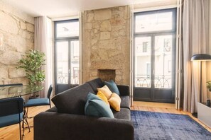 A living room with a stone wall, a sofa with cushions, a glass table with chairs, and a view through a glass door.