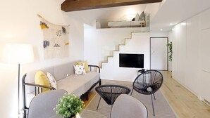 Un saló modern amb un sofà, dues butaques, una televisió i una escala que mena a un pis superior.