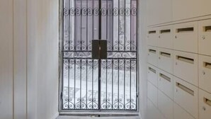 A narrow hallway with a patterned floor, a metal gate with decorative bars, and a row of white lockers on the right.