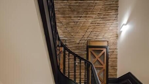 A spiral staircase with wooden steps and black railings, leading to a landing with a wooden door and a textured wall.