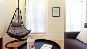 A modern living room with a hanging chair, a sofa, a black coffee table with a book, and a framed picture on the wall.