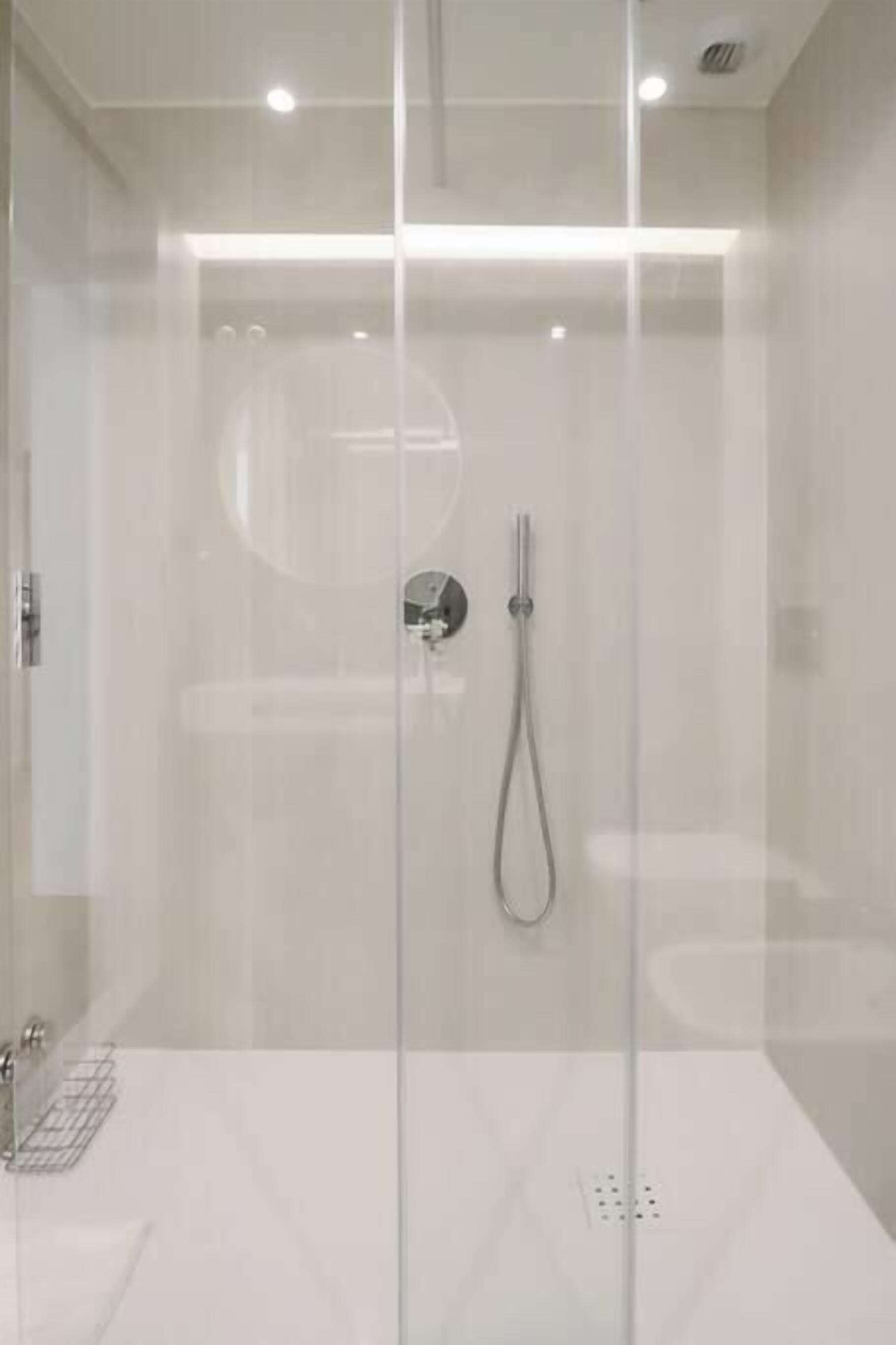 Una ducha moderna con puerta de vidrio, cabezal de ducha manual y panel de control.