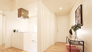 A modern hotel room with a wooden floor, a white partition, a black-framed TV stand, and a framed picture on the wall. - HM - Ribeira São João Apartment - 2D (Porto)