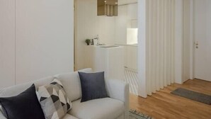 A modern living room with a sofa and a kitchen in the background. - HM - Ribeira São João Apartment - 2D (Porto)