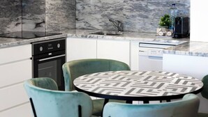 Una cocina moderna con salpicadero de mármol, lavavajillas integrado y una mesa redonda con sillas estampadas.