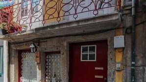 Un edificio con puerta roja, un balcón con barandilla de hierro forjado y fachada de piedra.